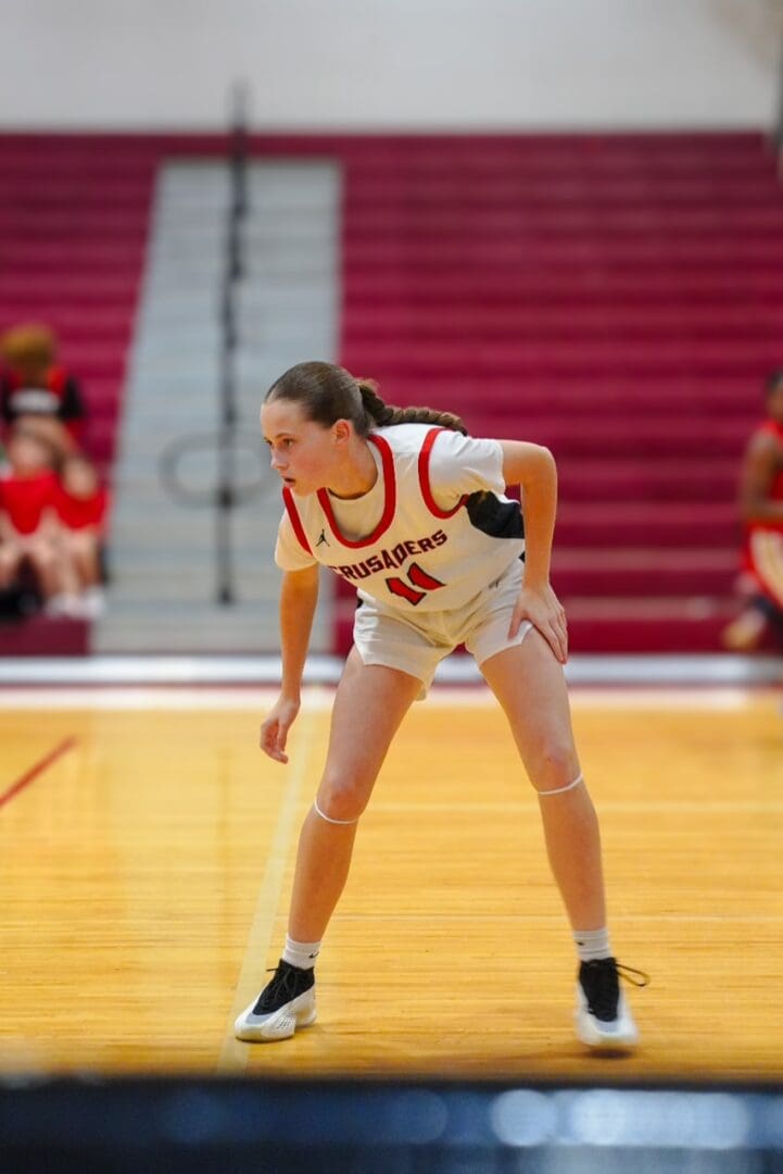 Female basketball player in white and red uniform on court, focused during game.